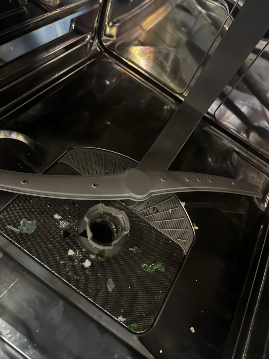 The interior of a dishwasher with the spray arm and filter exposed, food debris around the sump — a real repair diagnosis